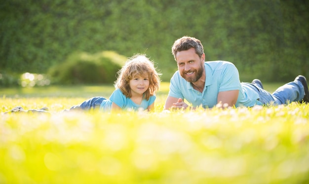 父と息子の男の子の幸せな家族は、夏の公園の緑の芝生の子供時代にリラックスします