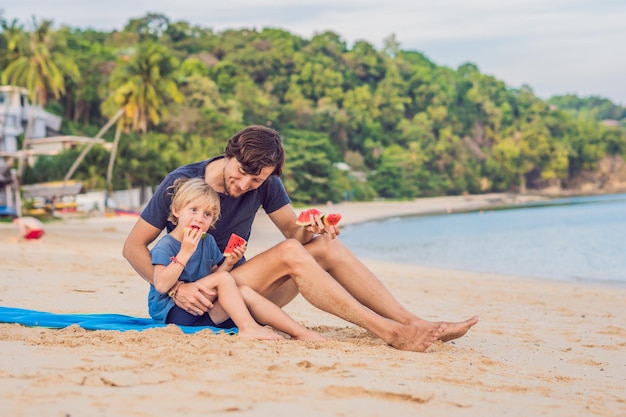 Famiglia felice padre e figlio che mangiano un'anguria sulla spiaggia. i bambini mangiano cibo sano.