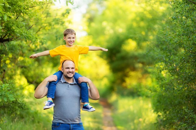 Счастливая семья: отец и сын гуляют в природе летом. Сын сидит на спине отца.