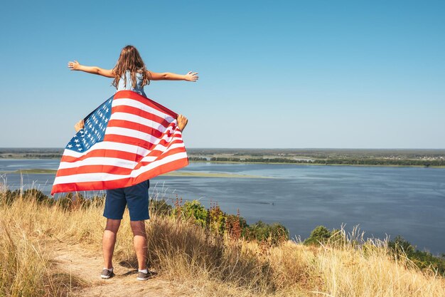 Happy family father with america flag and daughter sitting on fathers shoulders enjoy nature