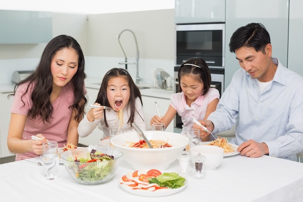 キッチンでスパゲッティランチを楽しむ4人の幸せな家族