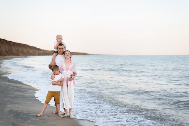 Счастливая семья из четырех человек обниматься на берегу моря. Родители, беременная мама и двое сыновей.