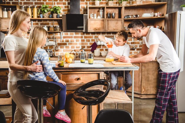 Photo happy family of four makes orange juice for breakfast in kitchen