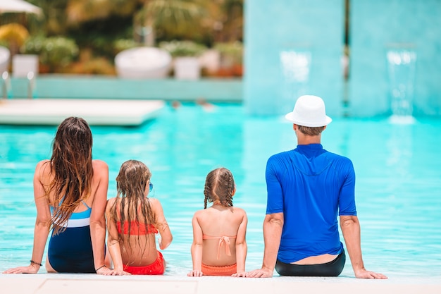 Happy family of four in outdoors swimming pool