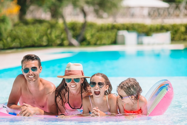 Happy family of four in outdoors swimming pool