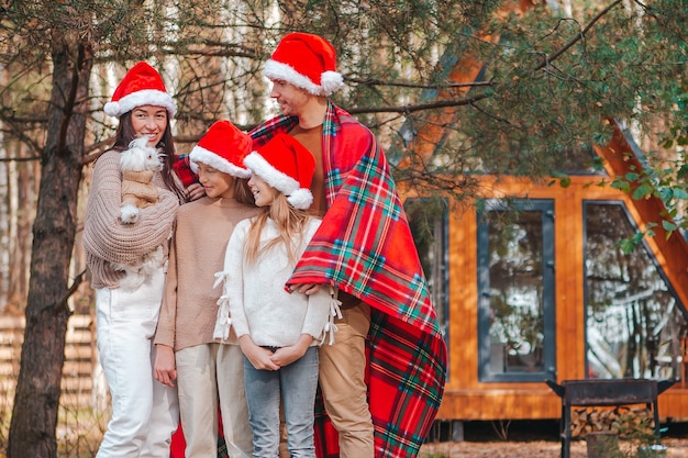 Happy family of four in Santa hat enjoying Christmas vacation. Parent with kids wrapped in a blanket