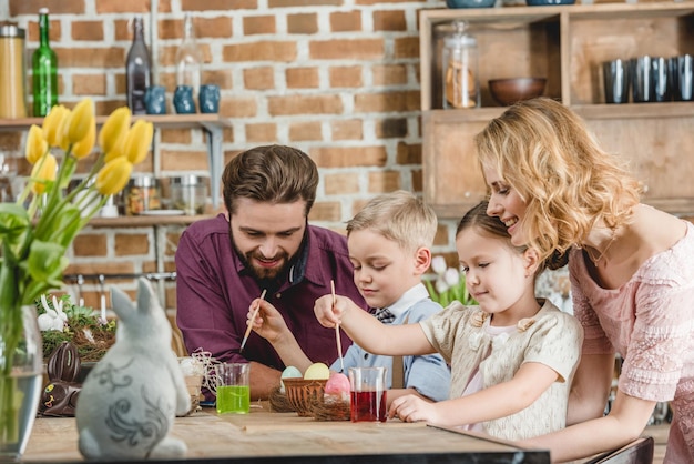 Happy family of four sitting at the table and painting Easter eggs