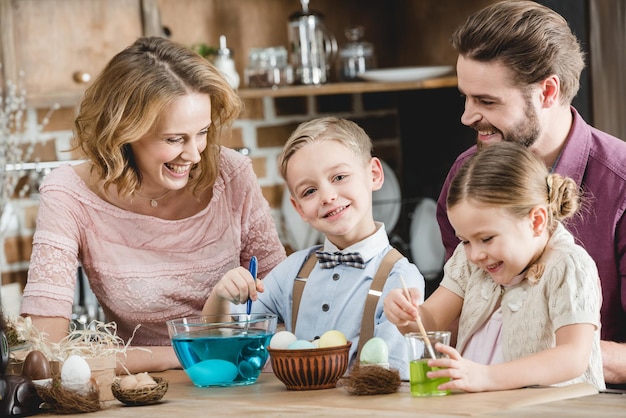 Happy family of four sitting at the table and painting eggs for Easter