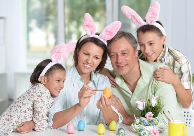 Happy family of four wearing bunny ears and painting Easter eggs at home