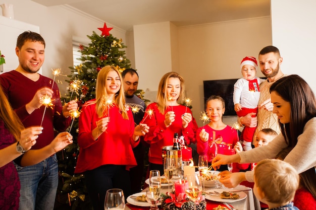 Happy family and friends waiting for Christmas while standing near New Year tree with sparklers in hands. Merry Christmas.