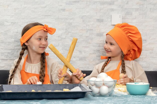 Happy family Funny girls kids in orange chef uniform are preparing the dough bake cookies in the kitchen Sisters children enjoy cooking food Warm relations