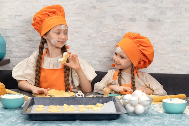 Happy family funny girls kids in orange chef uniform are preparing the dough bake cookies in the kitchen sisters children enjoy cooking food warm relations