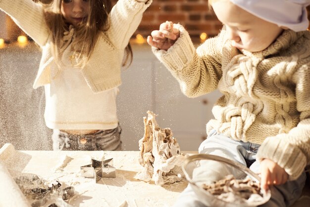 幸せな家族の面白い子供たちは台所で小麦粉で遊んで、生地を準備しています