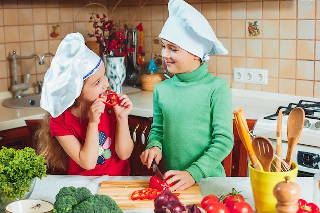 Happy family funny kids are preparing the a fresh vegetable salad in the kitchen