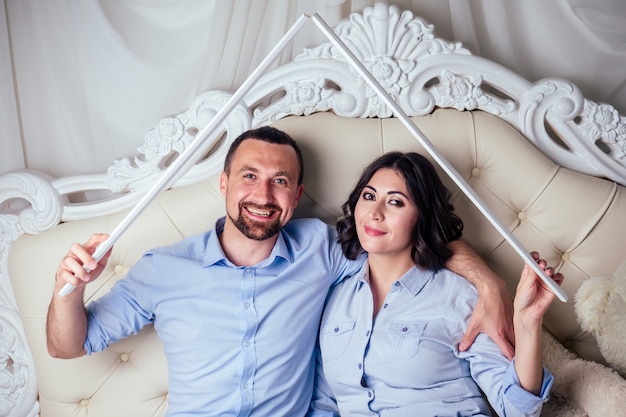 Happy family handsome man and charming woman together make the roof on bed in bedroom . concept of buying a house by newlyweds.