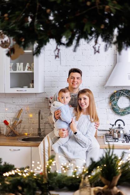 A happy family happy young couple with their little son in the\
kitchen decorated for the new year new year\'s interior in the\
kitchen christmas kitchen festive family atmosphere