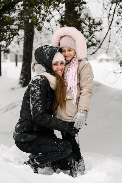 幸せな家族は冬の森で楽しんでいます。雪で抱きしめたり遊んだりする母と娘。家族の概念。一緒に時間を楽しむ