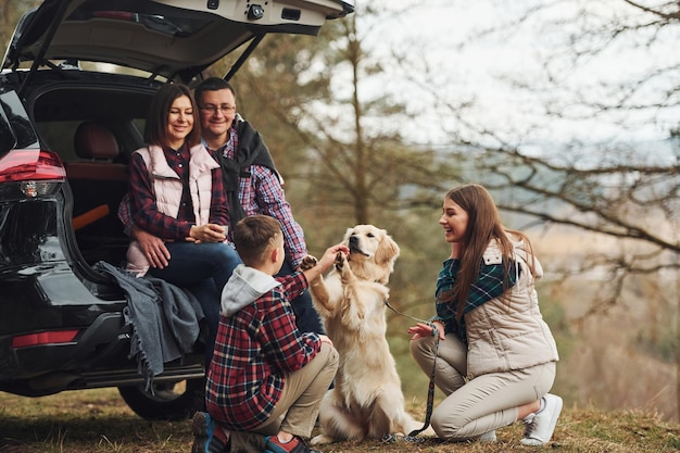 Happy family have fun with their dog near modern car outdoors in forest