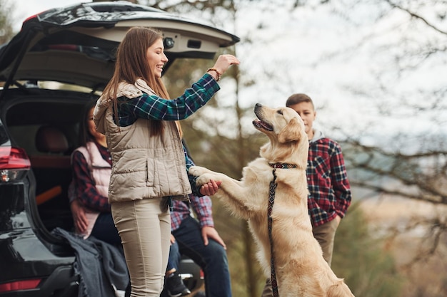 幸せな家族は森の中で屋外で現代の車の近くで彼らの犬と一緒に楽しんでいます