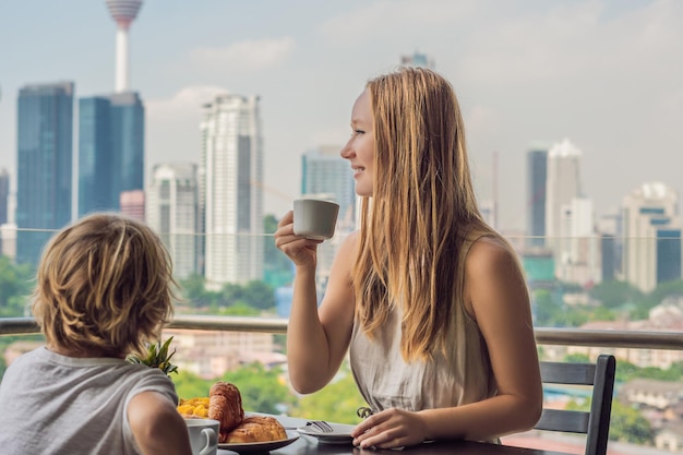 Famiglia felice facendo colazione sul balcone tavolo per la colazione con caffè, frutta e pane croissant su un balcone sullo sfondo della grande città