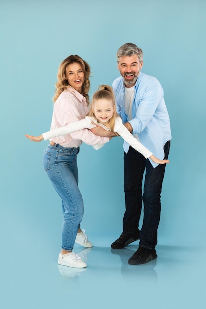 Happy family having fun parents holding daughter over blue background