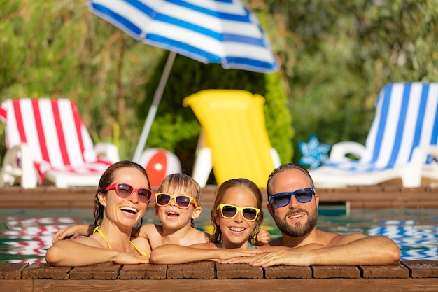 Счастливая семья, весело проводящая время на летних каникулах Отец, мать и дети, играющие в бассейне, концепция активного здорового образа жизни