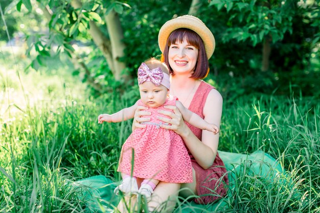 Una famiglia felice che fa un picnic nel giardino verde in una soleggiata giornata di primavera: una bella madre sorridente seduta sull'erba verde e la sua piccola figlia che ride sulle sue gambe