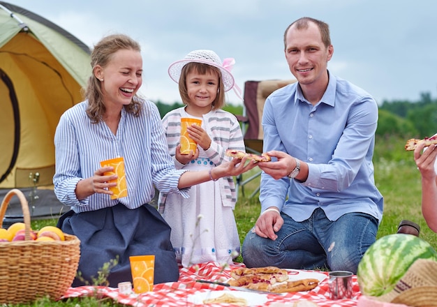 Happy family having picnic in meadow on a sunny day Family Enjoying Camping Holiday In Countryside