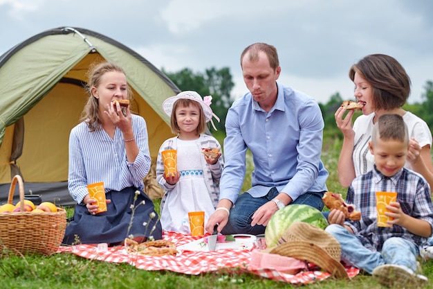 Happy family having picnic in meadow on a sunny day. Family Enjoying Camping Holiday In Countryside