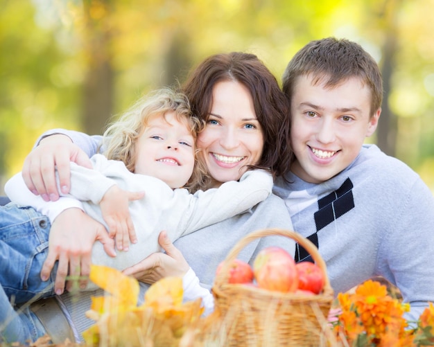 Happy family having picnic outdoors in autumn park against blurred leaves background