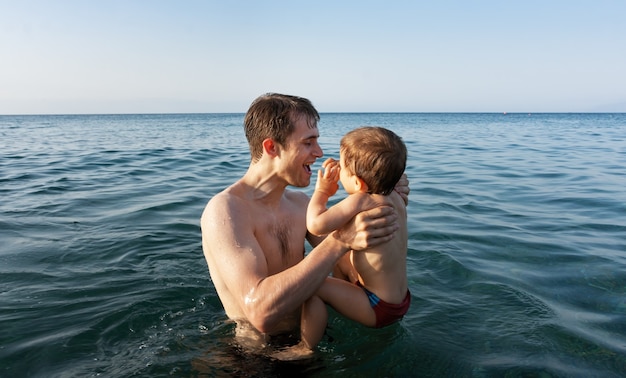 Famiglia felice e stile di vita sano. un giovane padre insegna a un bambino a nuotare nel mare