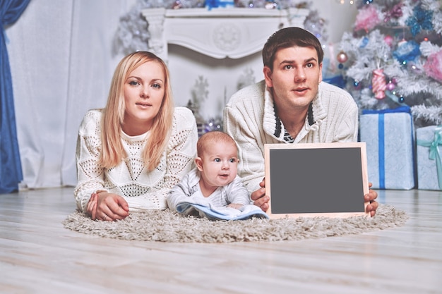 Happy family holding a blank Christmas card, lying on the carpet in a cozy living room . photo with copy space