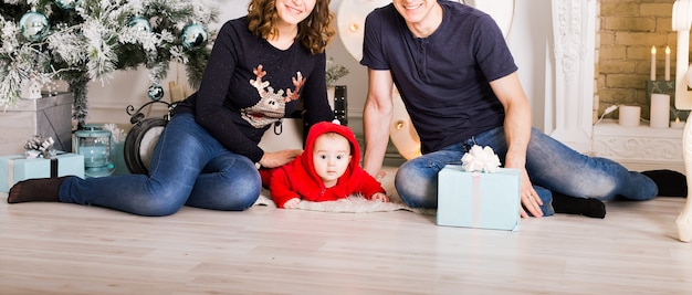 Happy family holding Christmas gifts near Xmas tree. Child, mother and father having fun at home.