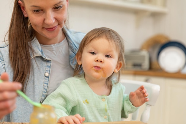 Happy family at home mother feeding her baby girl from spoon in kitchen little toddler child with