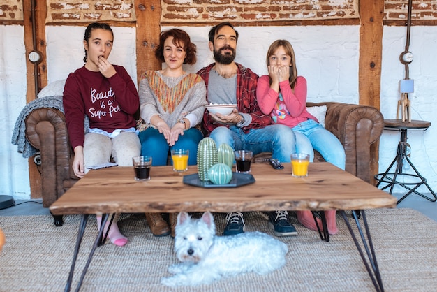 Счастливая семья дома смотрит фильмы на диване и ест попкорн
