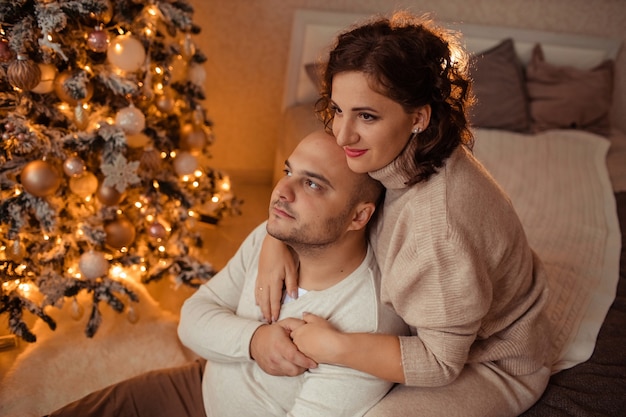 행복한 가족 남편과 아내가 크리스마스 트리 근처의 침대에 집에서 서로 포옹.