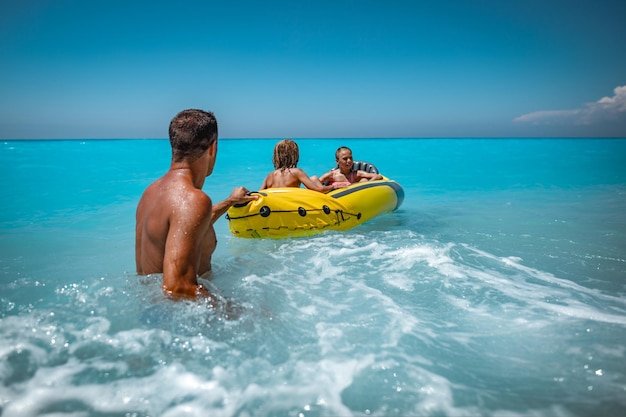 La famiglia felice si diverte a galleggiare in kayak giallo nell'acqua tropicale dell'oceano durante le vacanze estive. il padre fa la guardia ai bambini che guidano su un gommone.