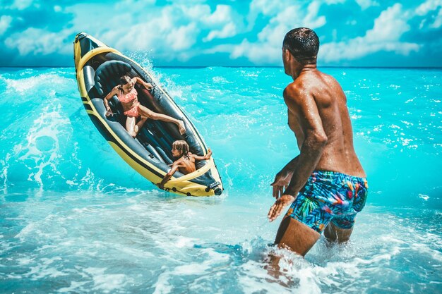 幸せな家族は夏休みの間に熱帯の海の水で黄色いカヤックに浮かんで楽しんでいます。父親はゴムボートで運転している子供たちを守っていて、波が彼らをはねかけています。