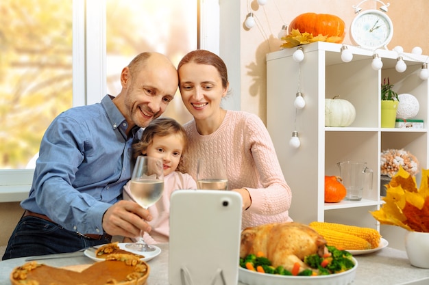 Una famiglia felice sta facendo una cena di ringraziamento, tenendo in mano un bicchiere di vino e salutando i genitori, in una videoconferenza