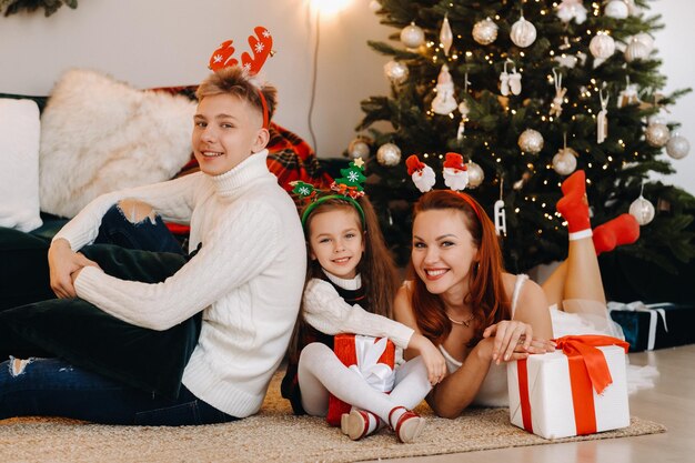 幸せな家族がクリスマスツリーの隣に、新年の贈り物を持って家の床に横たわっています