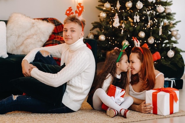 A happy family is lying on the floor of the house with New Year's gifts, next to the Christmas tree