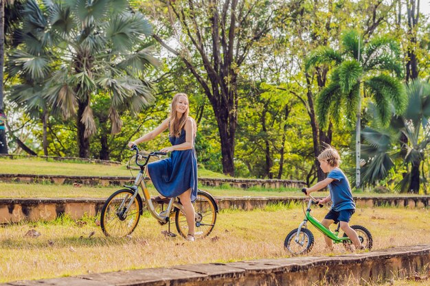 Happy family is riding bikes outdoors and smiling. Mom on a bike and son on a balancebike