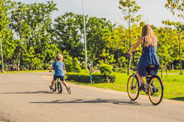 행복한 가족이 야외에서 자전거를 타고 웃고 있습니다. 자전거를 탄 엄마와 균형 자전거를 탄 아들