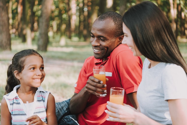 Happy family is smiling in the forest and drinking juice