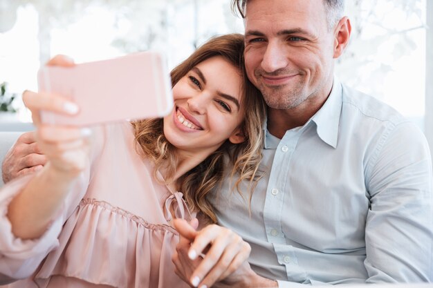 Famiglia felice di gioiosa coppia di sposi che fa selfie e si diverte insieme, mentre si incontra nel caffè della città