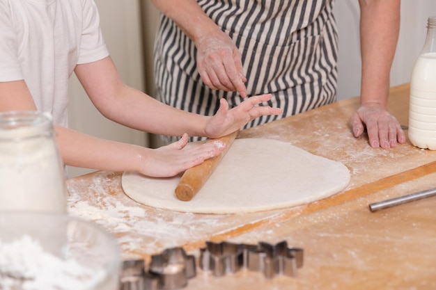 Happy family in kitchen grandmother granddaughter child hands roll out dough on kitchen table togeth