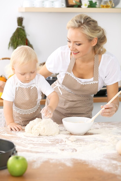 キッチンで幸せな家族。母の日のための休日のパイやクッキーを調理する母と子の娘、実際のインテリアでカジュアルなライフスタイルの写真シリーズ