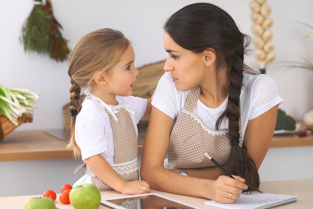 Happy family in the kitchen Mother and child daughter make menue for cooking tasty breakfest in the kitchen Little helper is ready for houshold job