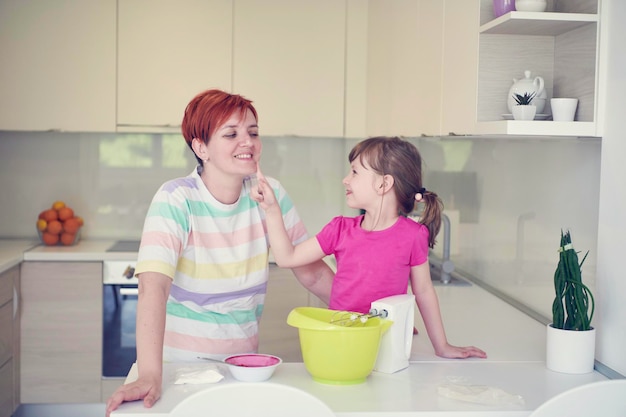 Happy family in the kitchen playing games and learning to cooking while staying at home during coronavirus covid-19 pandemic isolation. Mother and child daughter preparing the cake and cookies.