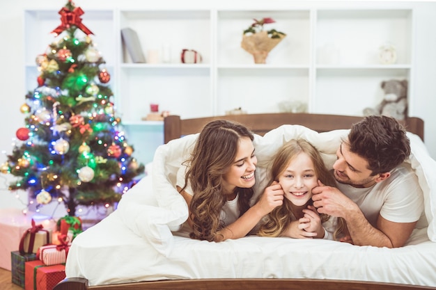 행복한 가족은 크리스마스 트리 근처의 침대에 누워 즐거운 시간을 보낸다